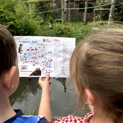 picture of children at Newquay Zoo holding a site map in front of a monkey enclosure