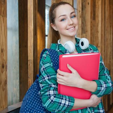 picture of a student with headphones around the next and carrying a red folder