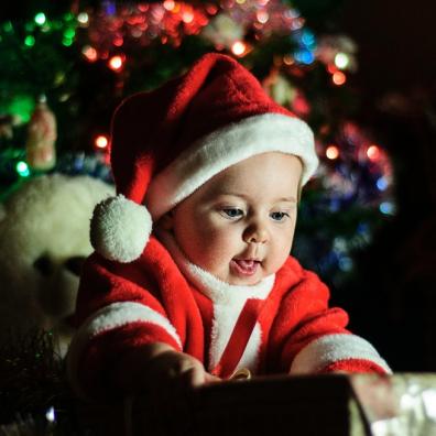 picture of a baby in front of a christmas tree dressed as santa