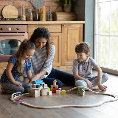 picture of a woman sat on a kitchen floor playing with a train track with a boy and girl