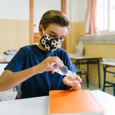 picture of a child wearing a face mask and using hand sanitiser in a school classroom