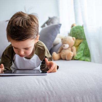 picture of a boy laying on a bed watching a tablet device