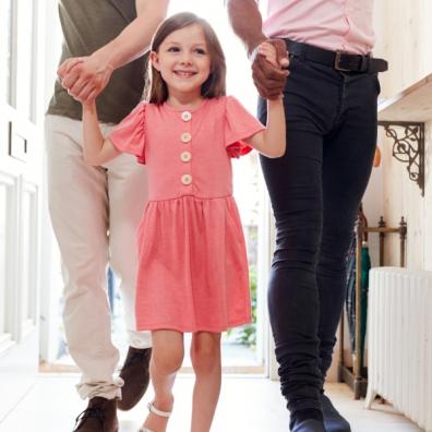 picture of a happy child in a pink dress walking into a house holding hands with grown ups