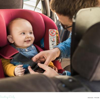 picture of a happy baby being strapped into a car seat in a car by their parent