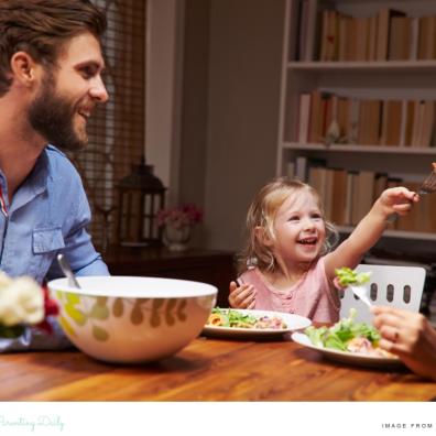 picture of a happy toddler sat at the table eating a meal with her family