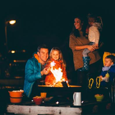 picture of a happy family sat around a fire pit with marshmallows