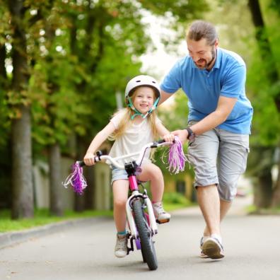 picture of a dad helping daughter learn how to ride a bike