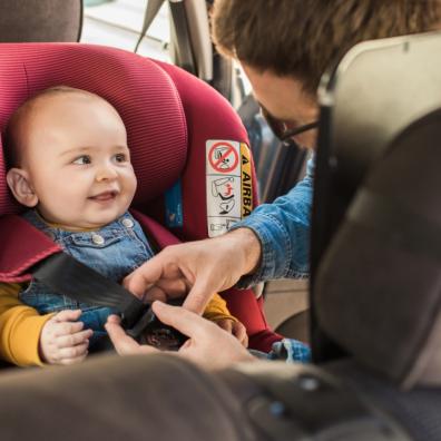 picture of a dad putting a happy baby in a red car seat