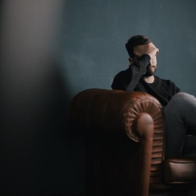 Photo of a man sat on a sofa with his head in his hands