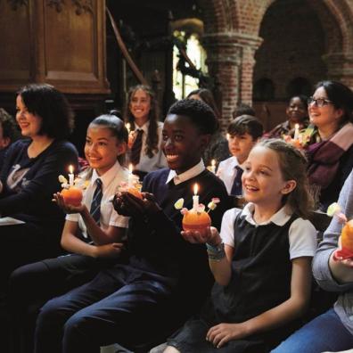 picture of children and adults sat in a church holding candles