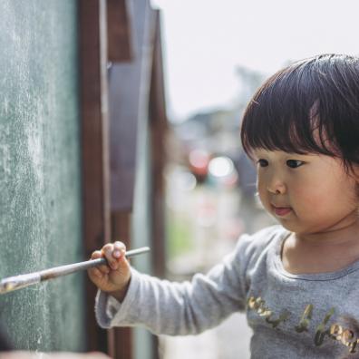 Picture of a little girl painting a fence outside