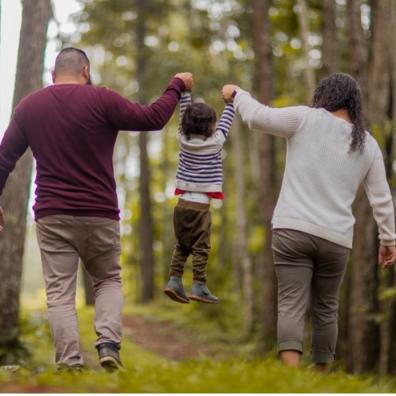 An image of a mother and a father holding hands with their son and swinging him up in the woods