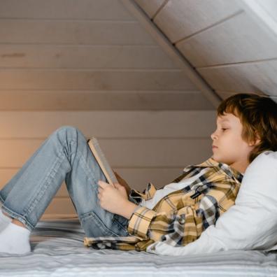 Child reading book sitting on bed