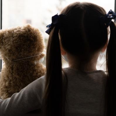 picture of a sad child with a teddy looking out of the window