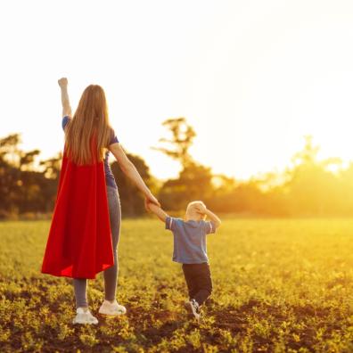 picture of a supermum wearing a cape with her child in a field